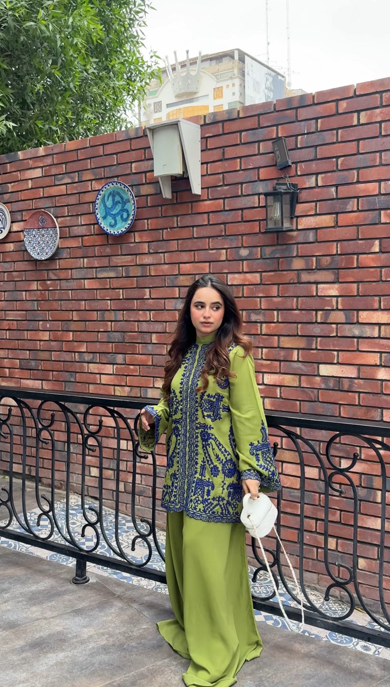 Woman wearing green embroidered designer 2-piece suit with intricate navy blue threadwork and wide-leg trousers by Momina Ammar Clothing, a luxury Pakistani brand offering worldwide delivery to UK, UAE, USA, and Canada."
