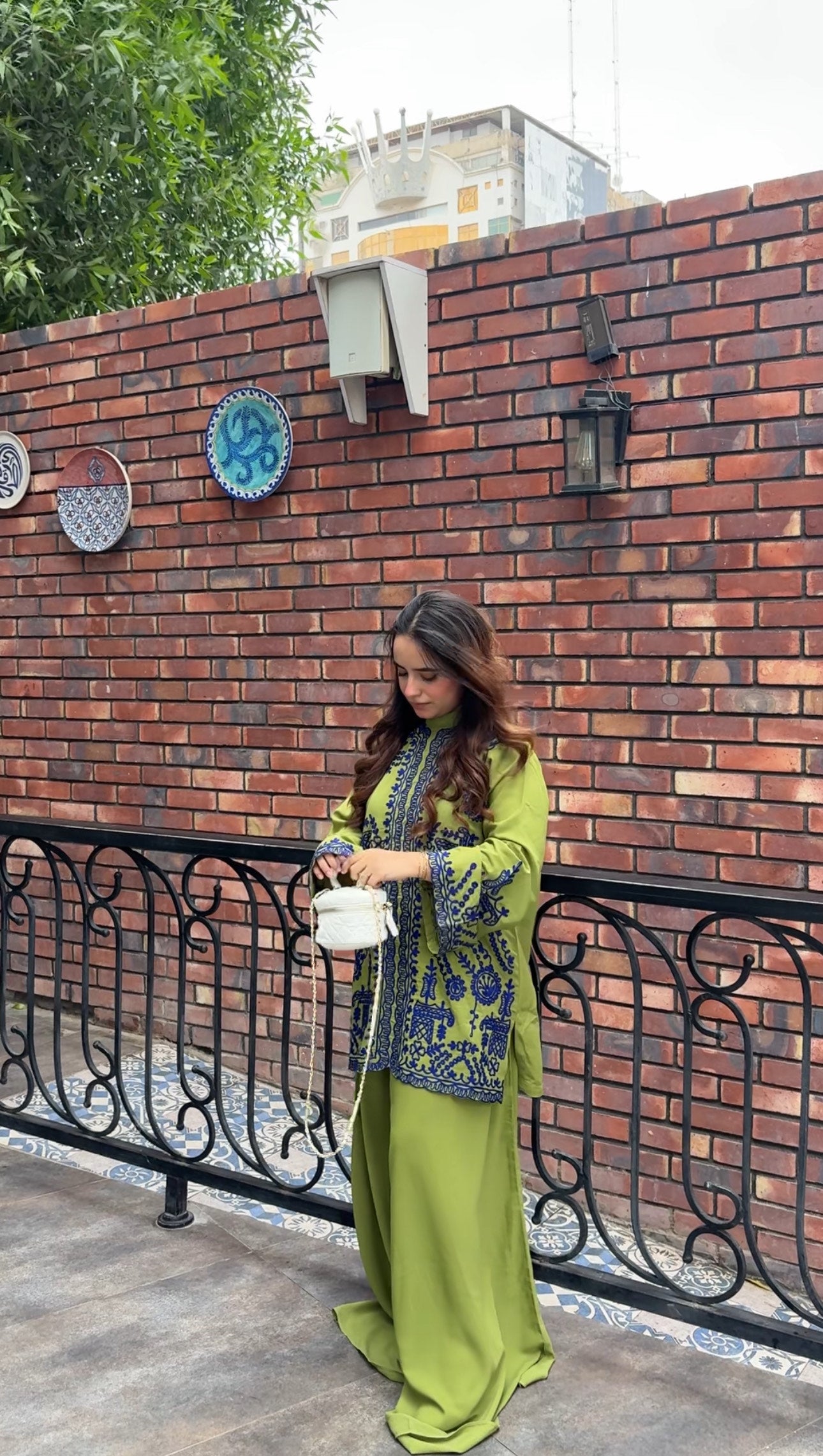 Woman wearing green embroidered designer 2-piece suit with intricate navy blue threadwork and wide-leg trousers by Momina Ammar Clothing, a luxury Pakistani brand offering worldwide delivery to UK, UAE, USA, and Canada."