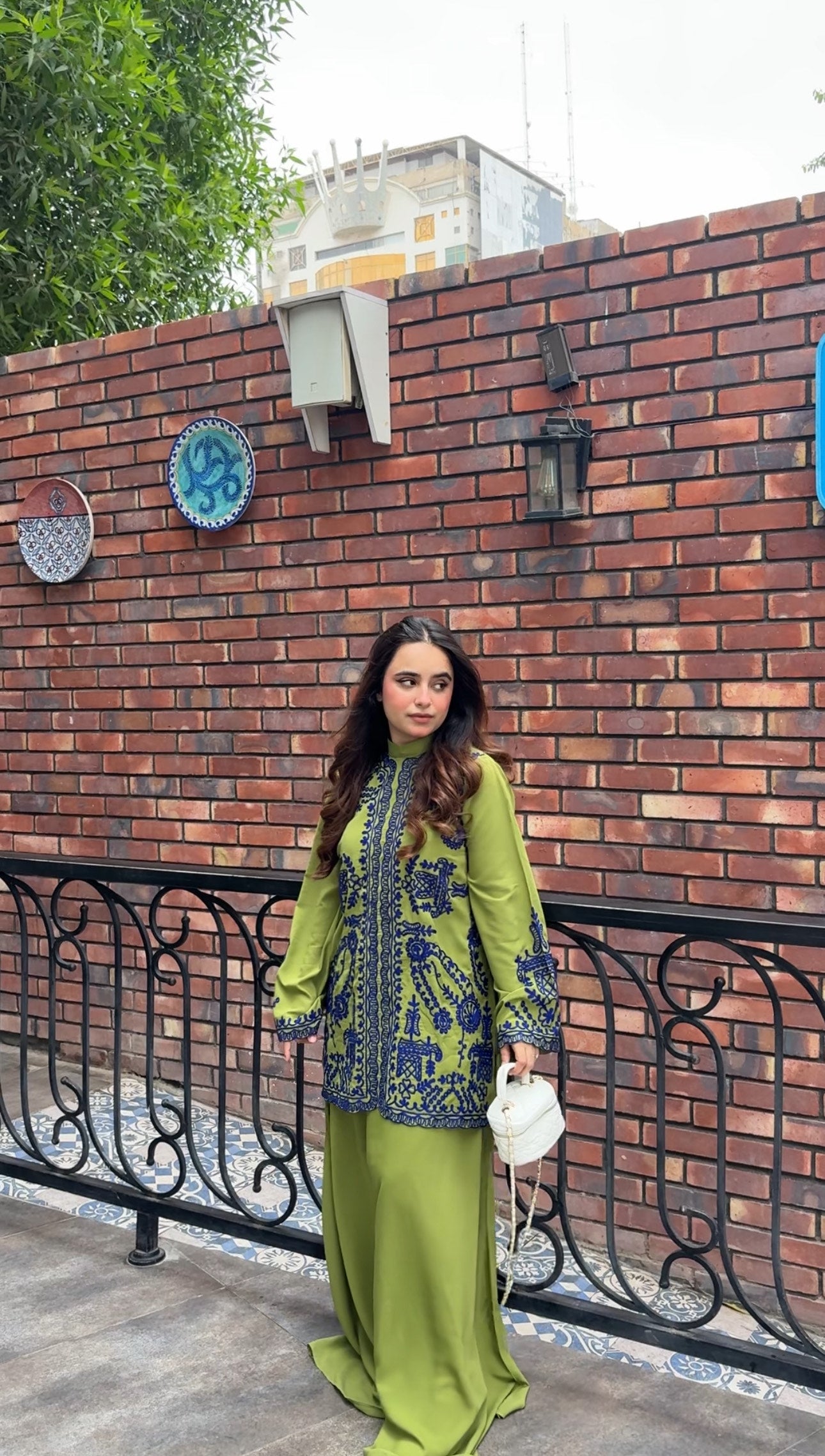 Woman wearing green embroidered designer 2-piece suit with intricate navy blue threadwork and wide-leg trousers by Momina Ammar Clothing, a luxury Pakistani brand offering worldwide delivery to UK, UAE, USA, and Canada."