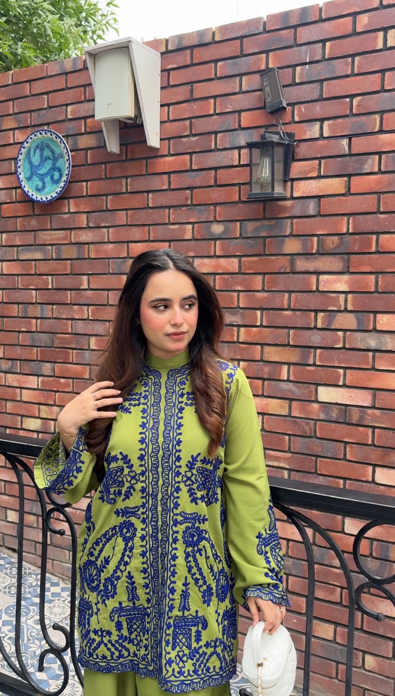 Woman wearing green embroidered designer 2-piece suit with intricate navy blue threadwork and wide-leg trousers by Momina Ammar Clothing, a luxury Pakistani brand offering worldwide delivery to UK, UAE, USA, and Canada."