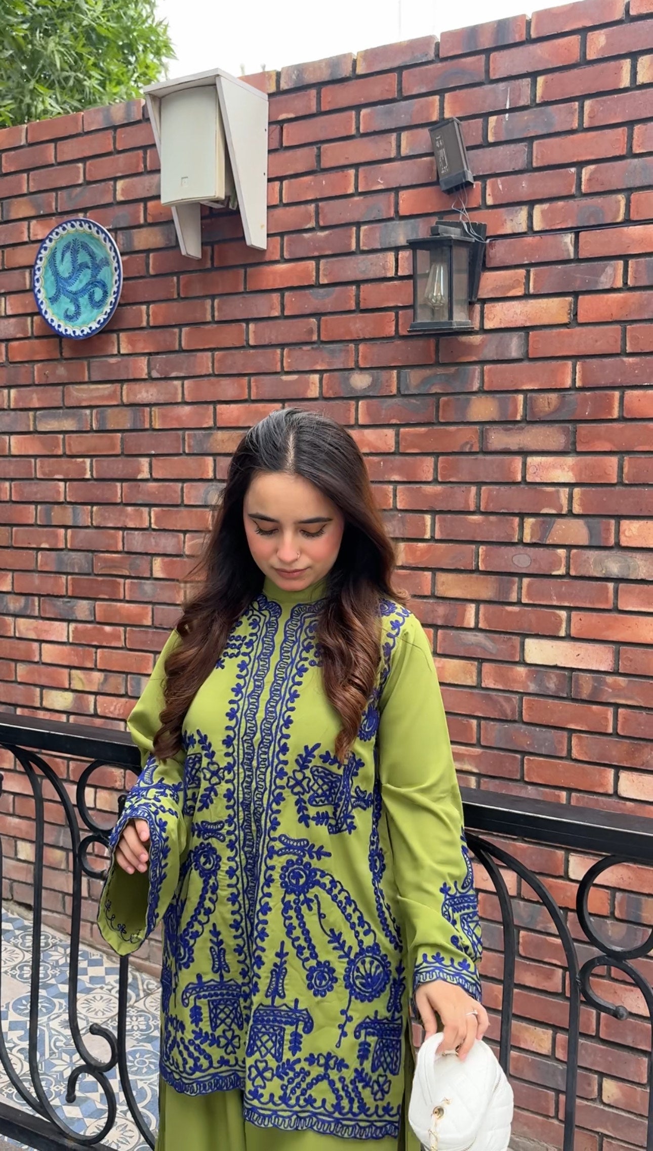 Woman wearing green embroidered designer 2-piece suit with intricate navy blue threadwork and wide-leg trousers by Momina Ammar Clothing, a luxury Pakistani brand offering worldwide delivery to UK, UAE, USA, and Canada."